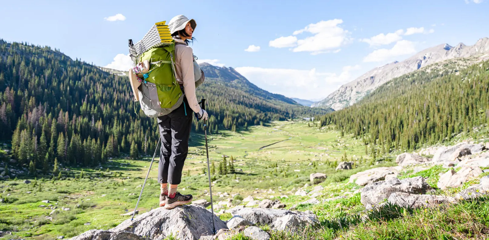 Woman wearing an Aarn Pack standing on a rock in the mountains