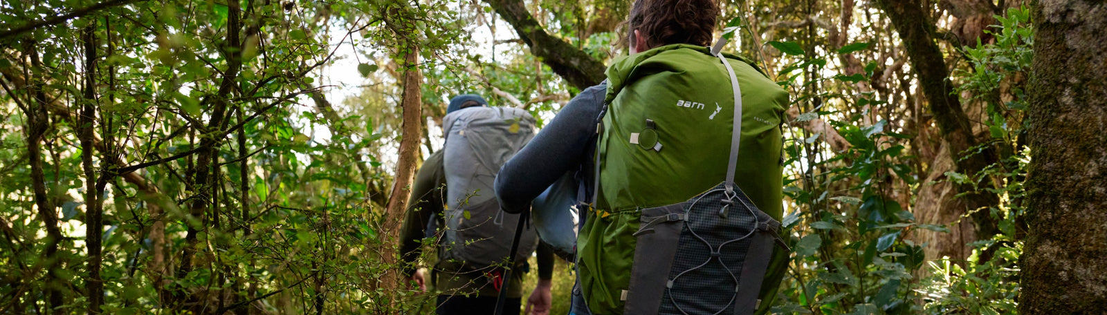 A woman and a man are walking through a forest in New Zealand while wearing their comfortable Aarn hiking backpacks. 