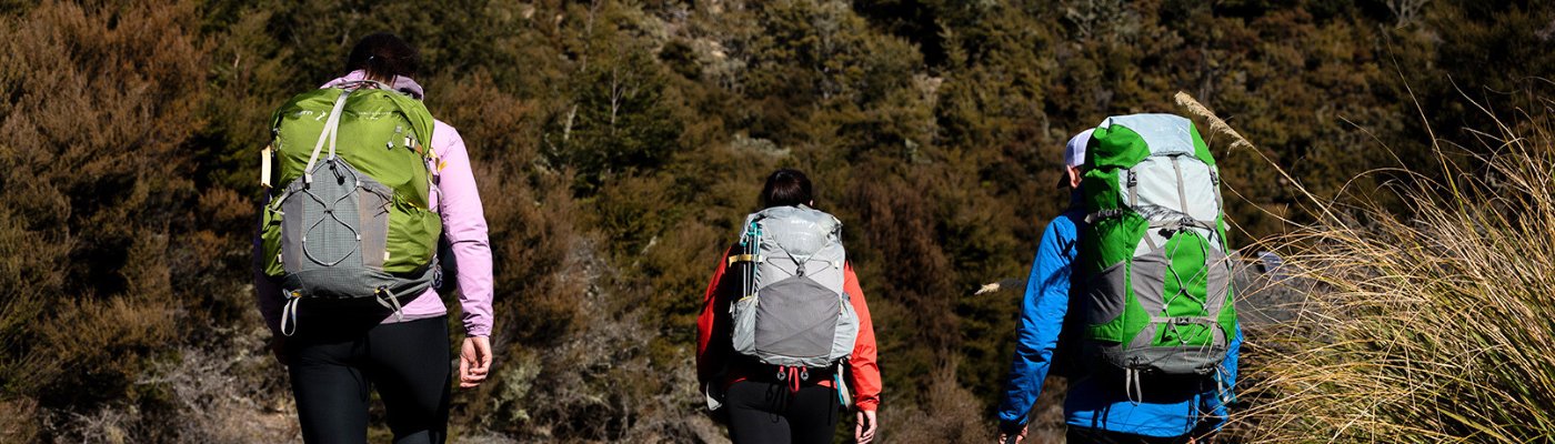 Two women and one man are hiking through the backcountry in New Zealand with Aarn hiking packs on. 