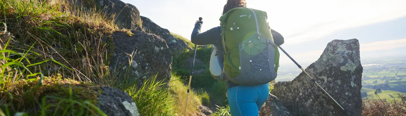 A woman is walking up hill in New Zealand. She's carrying an Aarn Featherlite freedom with front pockets. 